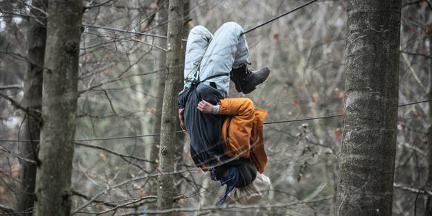 Ein Mensch hängt in Seilen zwischen Bäumen