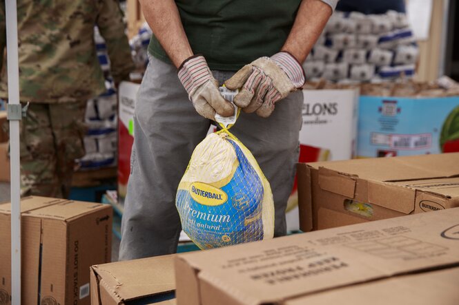 Ein Mann trägt Arbeitshandschuhe und hat einen verpackten Truthahn in den Händen