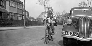 Rennradfahrerin fährt neben einem Auto in London 1938
