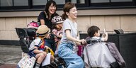 Zwei Frauen mit Fahrrädern auf denen sie drei Kinder transporieren zusammen mit jeder Menge Taschen