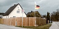 Ein Wohnhaus hinter einem Bretterzaun mit Deutschland-Fahne.