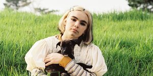 Die neuseeländische Popsängerin Benee mit einem Hundewelpen im Arm vor einer grünen Wiese