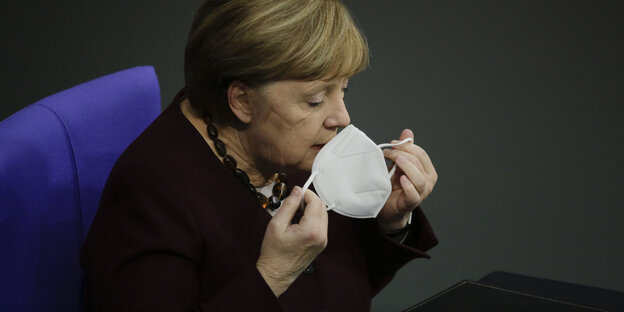 Merkel setzt sich eine Maske auf