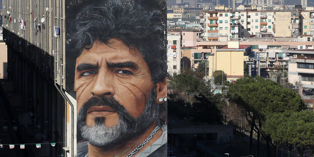 Ein Porträt von Maradona ist in riesigen Dimensionen an eine Hauswand gemalt, dahinter sieht man die Stadt Neapel