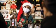 Eine junge Frau mit mundschutz und Weihnachtsmütze ugeben von Weihnachts-Dekoartikeln