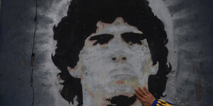 Ein Wandbild von Maradona, darauf die Hand von einem Fan