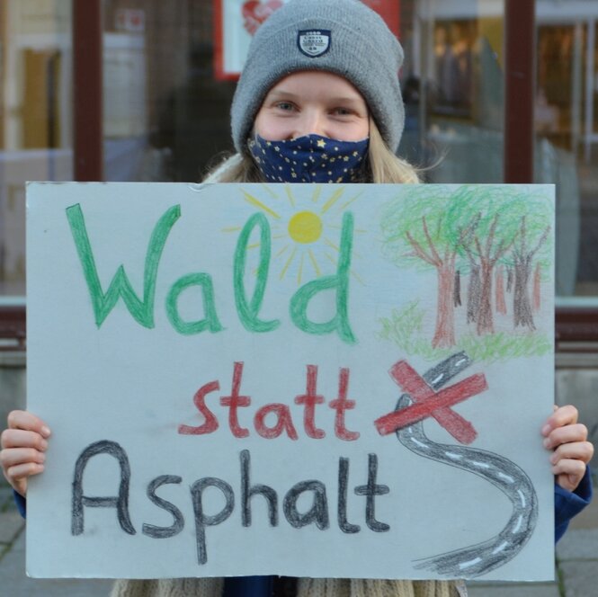 Helena Eckhoff trägt eine Maske und ein Protestplakat