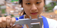 Eine junge Vietnamesin in einer Werkstatt. Sie misst ein Werkstück aus.
