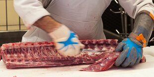 die Hände eines Metzgers mit Handschuhen der frisches Fleisch zerkleinert