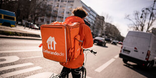 Ein lieferando Essenslieferdienst Fahrer ist mit seinem Rucksack auf einem Fahrrad