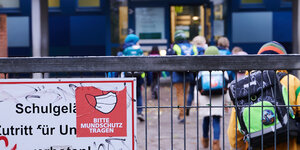Ein Gittertor und Schulkinder dahinter: „Bitte Mundschutz tragen“ steht am Eingang zu einer Grundschule in Friedrichshain