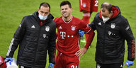 Bayern-Spieler Lucas Hernández wird im Spiel gegen Bremen von zwei Medizinern verletzt vom Platz geführt und verzieht das Gesicht