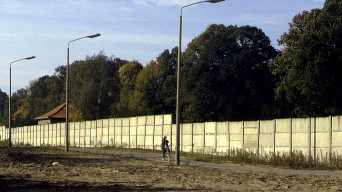 Franz John steht im Grenzstreifen und sitzt auf seinem Fahrrad mit der Videokamera