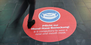 ein Aufkleber, der zum Maskentragen auffordert, im Bahnhof