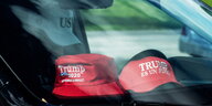Zwei rote Baseballmützen mit "Trump"-Aufschrift hinter einer Autoscheibe