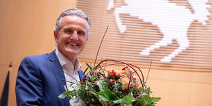 Ein Mann mit grauen Haaren im blauen Anzug mit Blumenstrauß