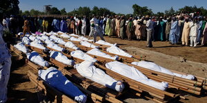 Dutzende Tote liegen in weißen Tüchern eingehuellt liegen in Borno, Nigeria auf dem Boden - es stehen viele Menschen um die Leichen herum