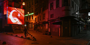 Ein Mann läuft nachts durch eine menschenleere Straße in Istanbul vor einem leuchtenden Schild mit der türkischen Flagge