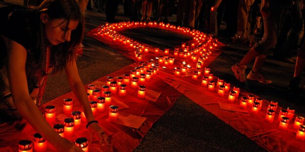 Ein Frau stellt Kerzen in Form einer rote Schleife als Solidaritätssymbol mit HIV Infizierten auf