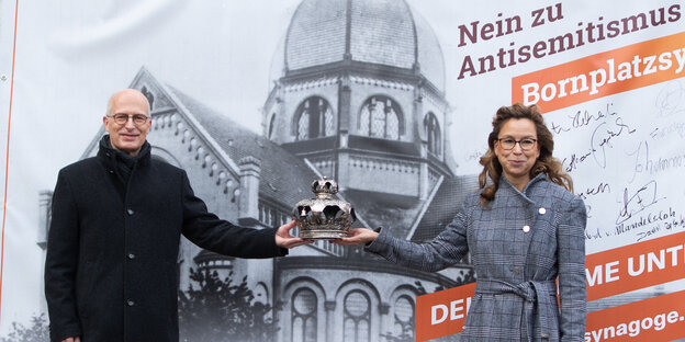 Peter Tschentscher (SPD), Erster Bürgermeister von Hamburg, und Carola Veit (SPD), Präsidentin der Bürgerschaft, stehen vor einem Plakat mit der Aufschrift ?"Nein zu Antisemitismus. Ja zur Bornplatzsynagoge"? und halten dabei eine Tora-Krone