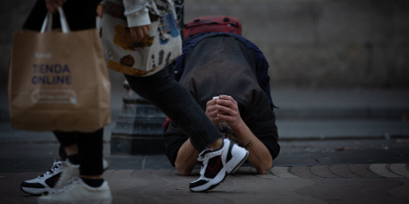 Spanien, Barcelona: Ein Mann bettelt auf der Straße inmitten der zweiten Welle der Corona-Pandemie, während Passanten mit Tüten von «online shops» an ihm vorbeigehen. Die regionale Regierung setze bis zum 23. November Anti-Corona-Maßnahmen in Kraft.