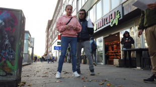 Eine Frau steht auf einem Bürgersteig, in ihrer Hand eine Brille