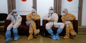 Erschöpfte Fachkräfte in Schutzkleidung sitzen nebeneinander in einem zum Krankenhaus umgewandeltem Ausstellungsraum in Moskau