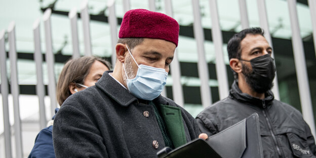 Der Imam Taha Sabri von der Neuköllner Begegnungsstätte nimmt an einer Friedenskundgebung des Zentralrates der Muslime teil. Er trägt einen Mundschutz und liest in einer Mappe