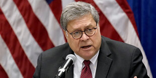 William Barr spricht vor einer US-Flagge in ein Mikrophon.