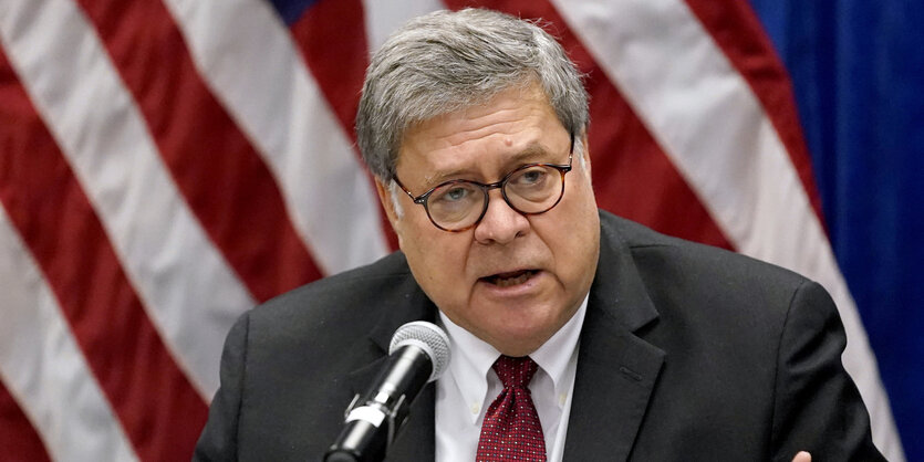 William Barr spricht vor einer US-Flagge in ein Mikrophon.