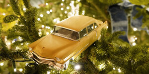 ein gelbes Spielzeugauto hängt als Baumschmuck in einer Weihnachtstanne