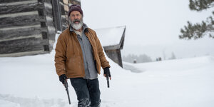 Mel Gibson als Fatman mit zwei Pistolen bewaffnet im Schnee.