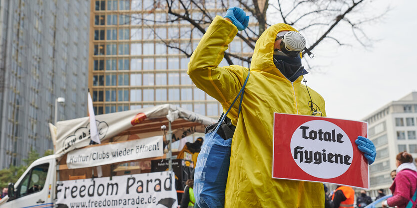 Ein Demonstrant mit gelbem Schutzanzur und einem Schild mit der Aufschrift "Totale Hygiene"