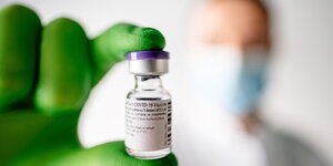 Ein Mann mit grünen Schutzhandschuhen hält eine kleine Ampulle des Corona-Impfstoffs von Biontech zwichen zwei Fingern