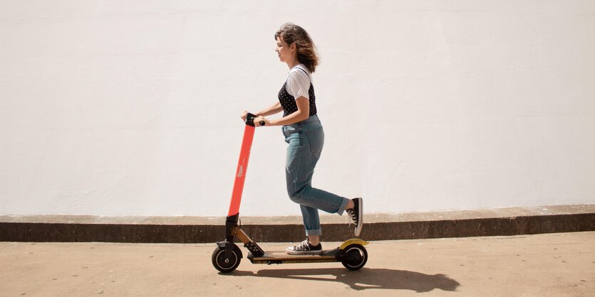 Eine Frau fährt auf einem E-Scooter auf dem Bürgersteig entlang