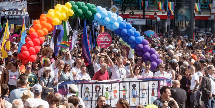 Menschenmenge mit gezeichneten Porträts unter einem Regenbogen aus Luftballons