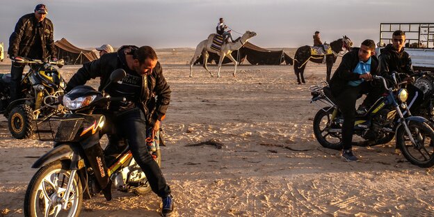 Dromedarreiter und Mopedfahrer in der Wüste