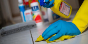 Eine Person in Gummihandschuhen putzt Fliesenboden in einer Wohnung