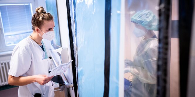 Zwei Krankenpflegerinnen auf der Covid-19-Station des Krankenhauses Bethel Berlin sprechen durch die Schleuse zum Krankenzimmer miteinander