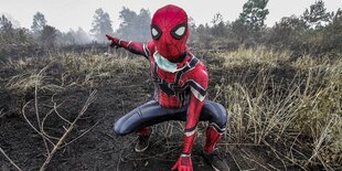 Eine Person im Spiderman-Kostüm kniet in einer abgebrannten Landschaft