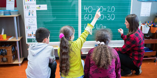 Auf dem Foto sind drei Schüler*innen von hinten fotografiert, die vor einer Tafel sitzen