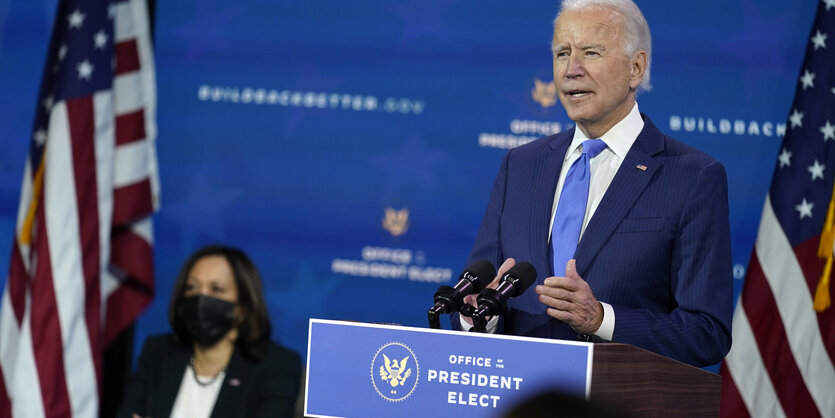 Joe Biden spricht an einem Redepult, im Hintergrund sitzt Kamala Harris