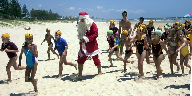 Weihnachtsmann am Strand umringt von Kindern in Badekkleidung