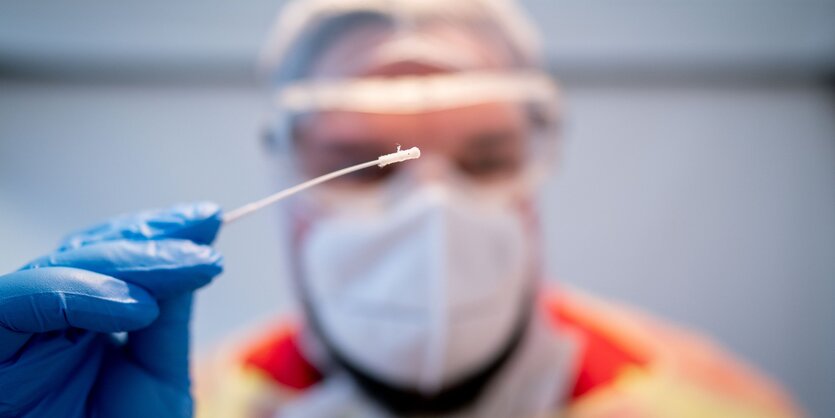 Ein Sanitäter mit Hygienemaske und Gesichtsvisier mit einem Abstrichstäbchen in der hand