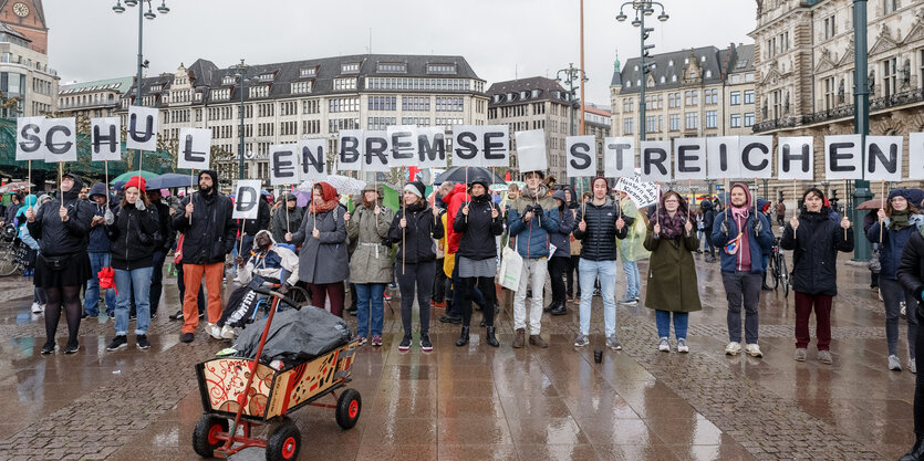 Menschen in einer Reihe stehem im Regen und halten Schilder