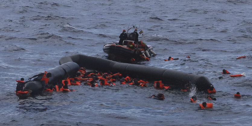 Ein Dutzend Menschen in Rettungswesten treiben im Meer und halten sich an Rettungsbojen fest.