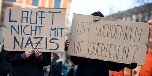 Zwei Gegendemonstrierende halten jeweils ein Protestplakat vor ihr Gesicht