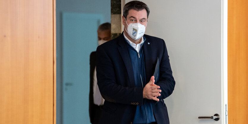 Markus Söder kommt durch eine Tür und reibt sich die Hände. Er trägt FFP2-Maske.