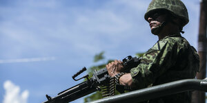 Ein Soldat in Tarnkleidung trägt ein Maschinengewehr.