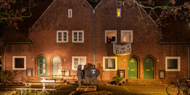 Polizei vor einem Doppelhaus aus Backstein, aus dem Leute ein Transparent hängen